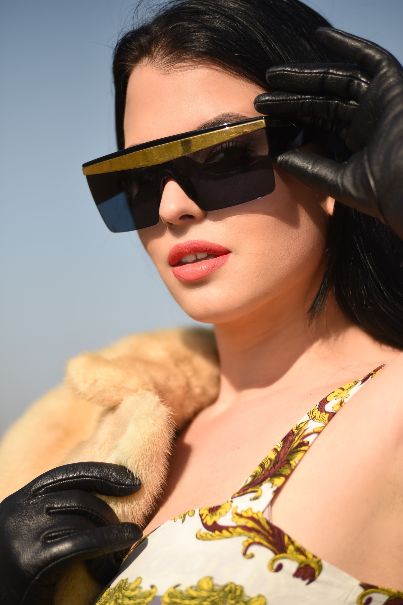 Model in black sunglasses and a tan coat against a clear blue sky