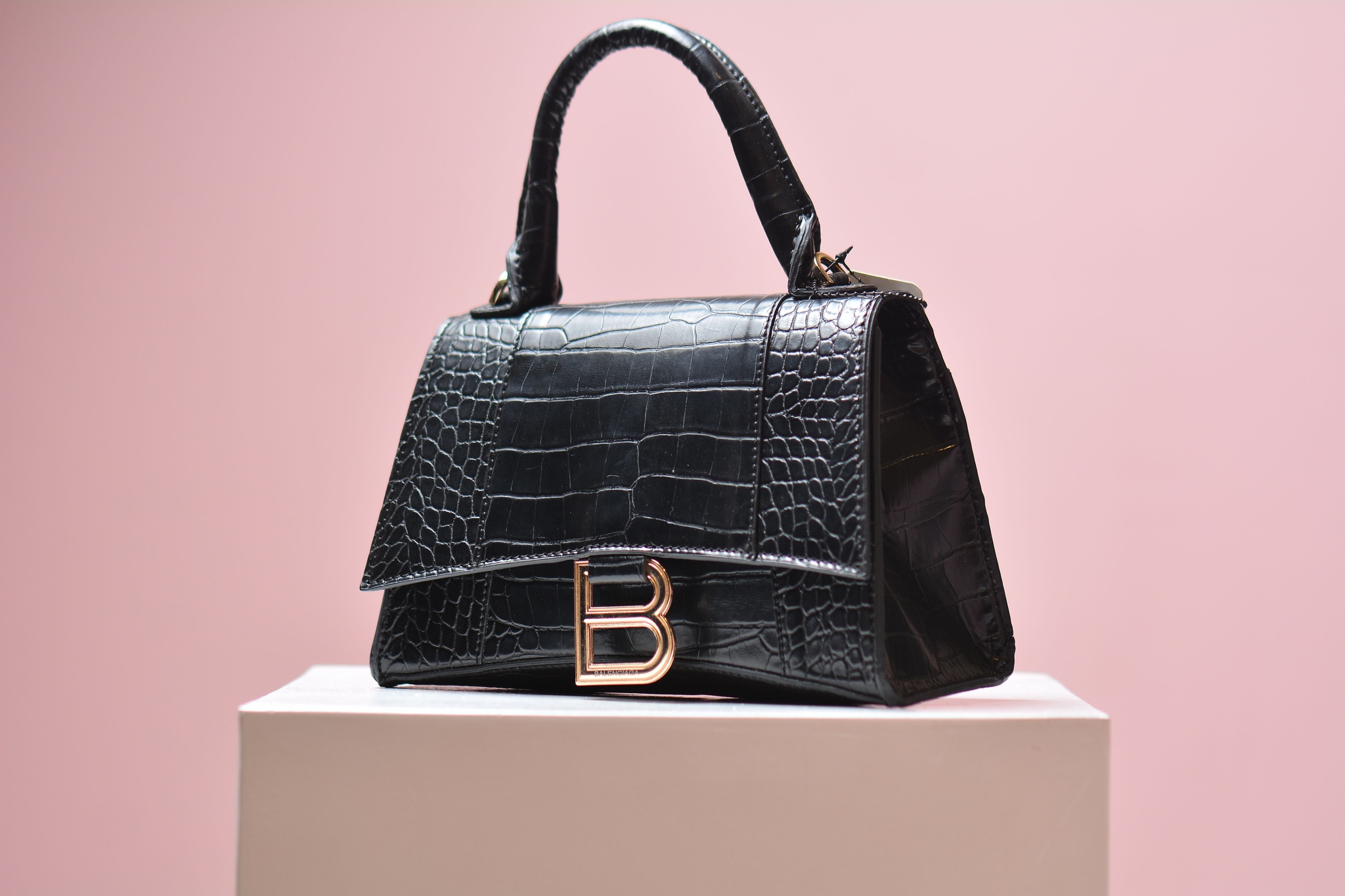 Black leather handbag with gold hardware, photographed against a pink backdrop