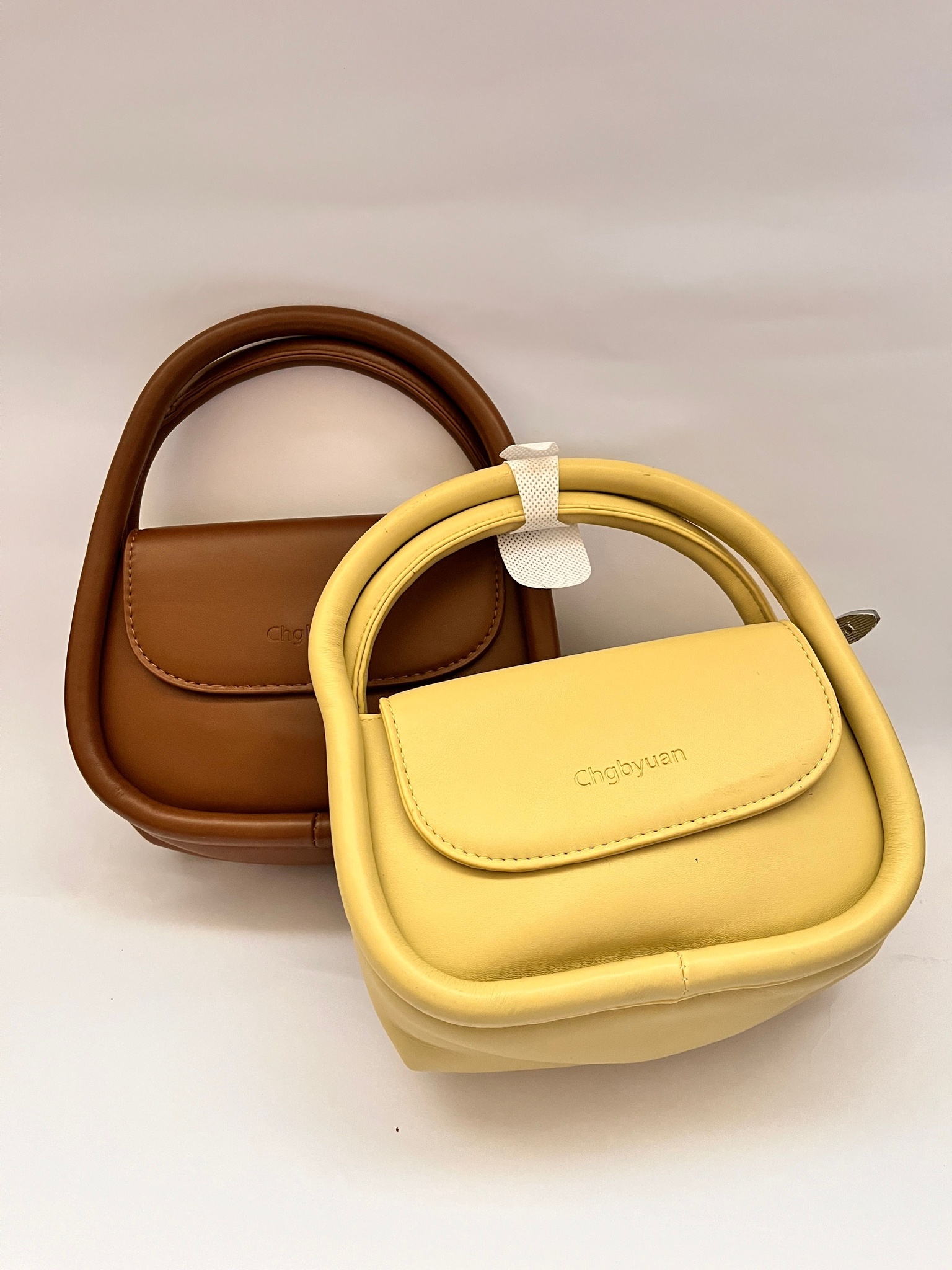 Two rounded mini handbags in warm brown and pale yellow