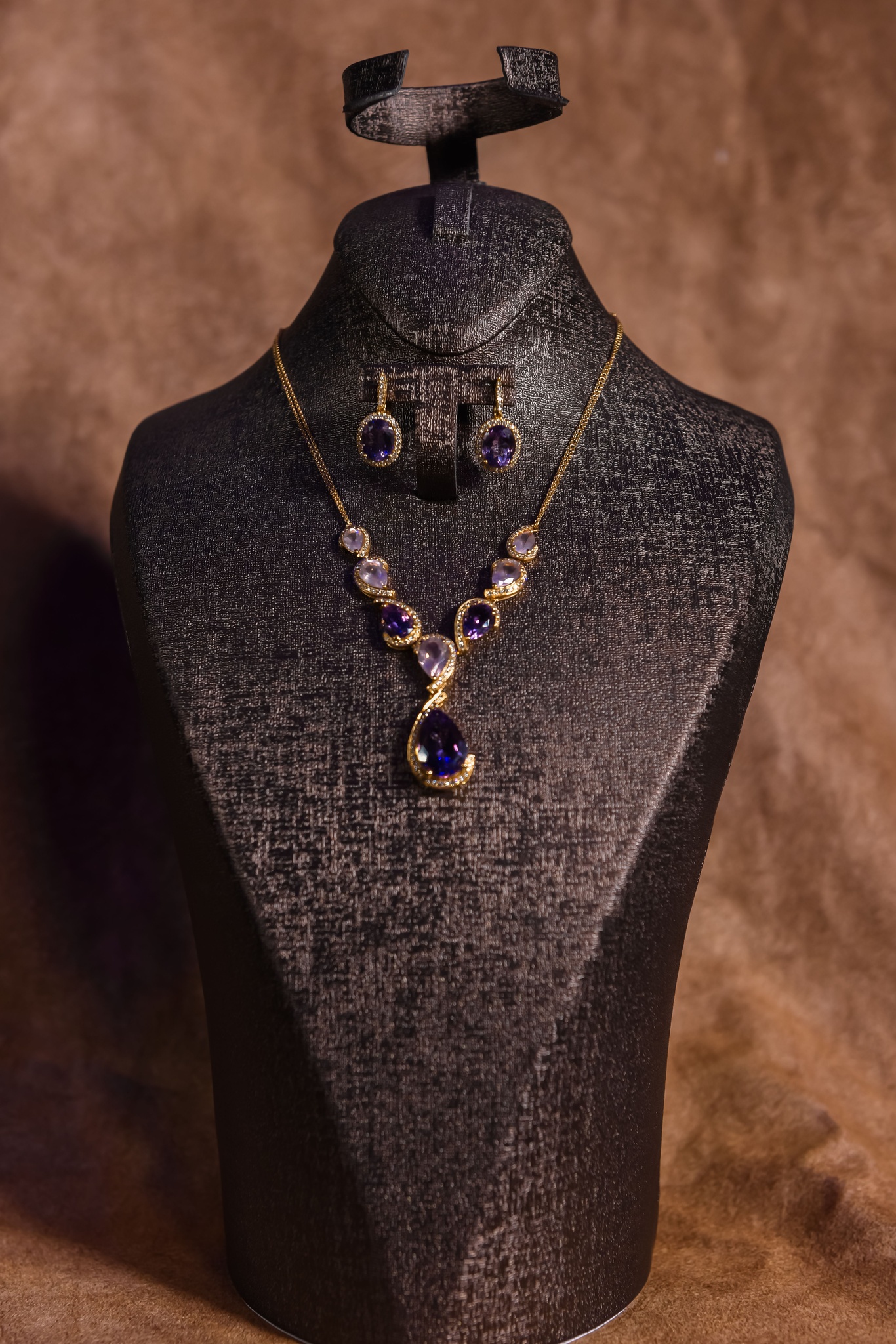 Gold necklace and earrings set with a teardrop stone on a black bust