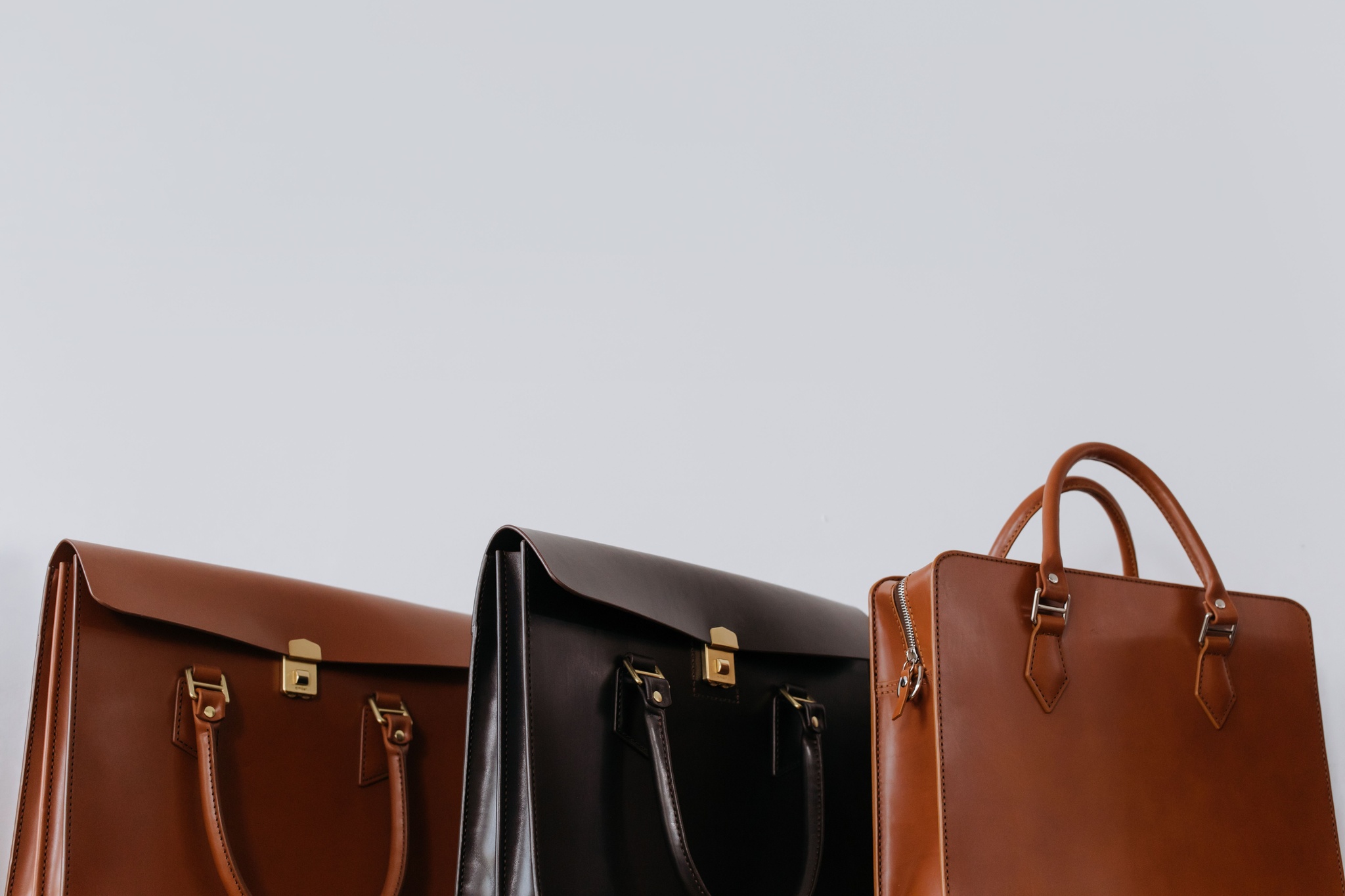 Three leather briefcases in graduated brown tones on a grey backdrop