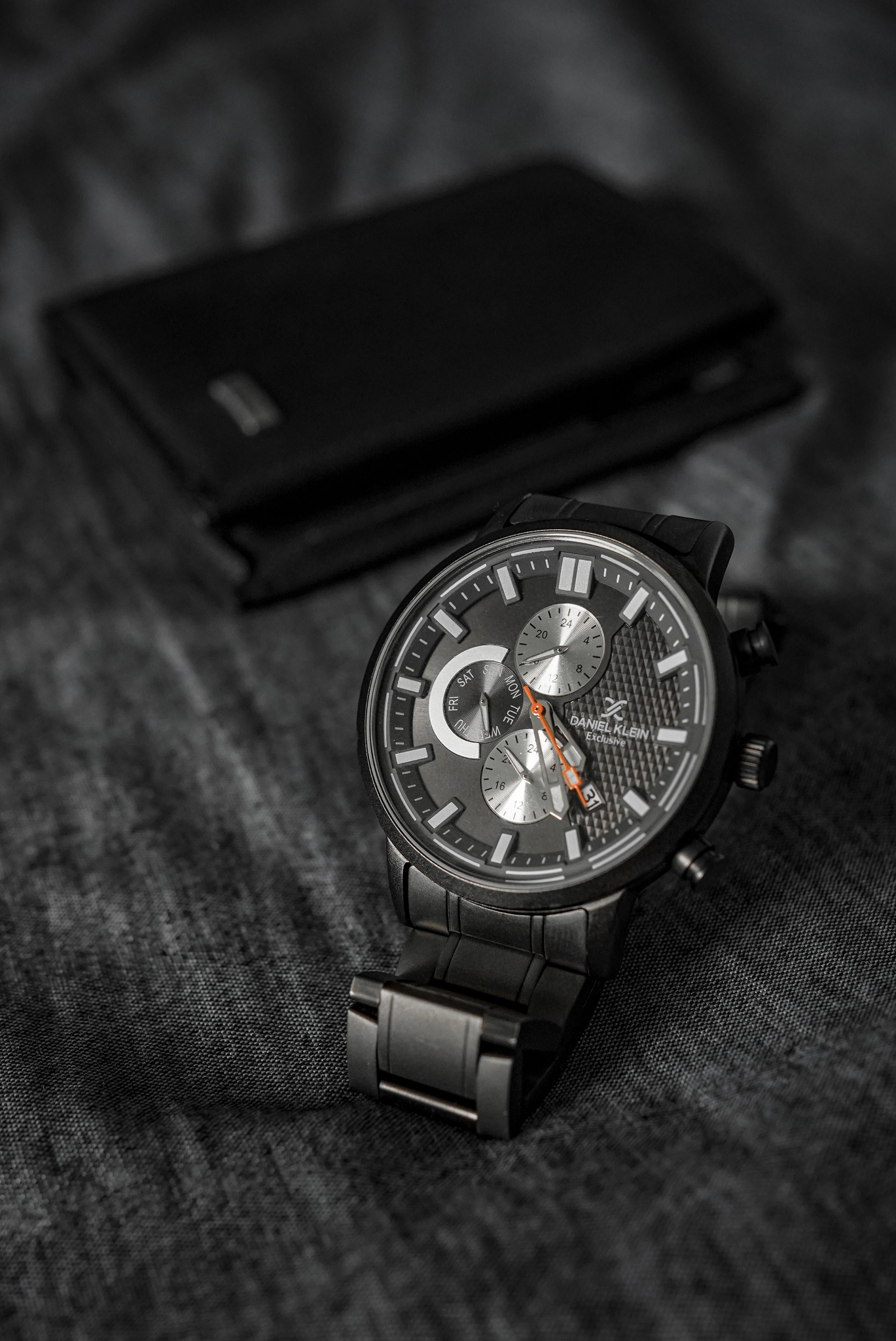 Black watch and a black leather wallet on dark grey fabric