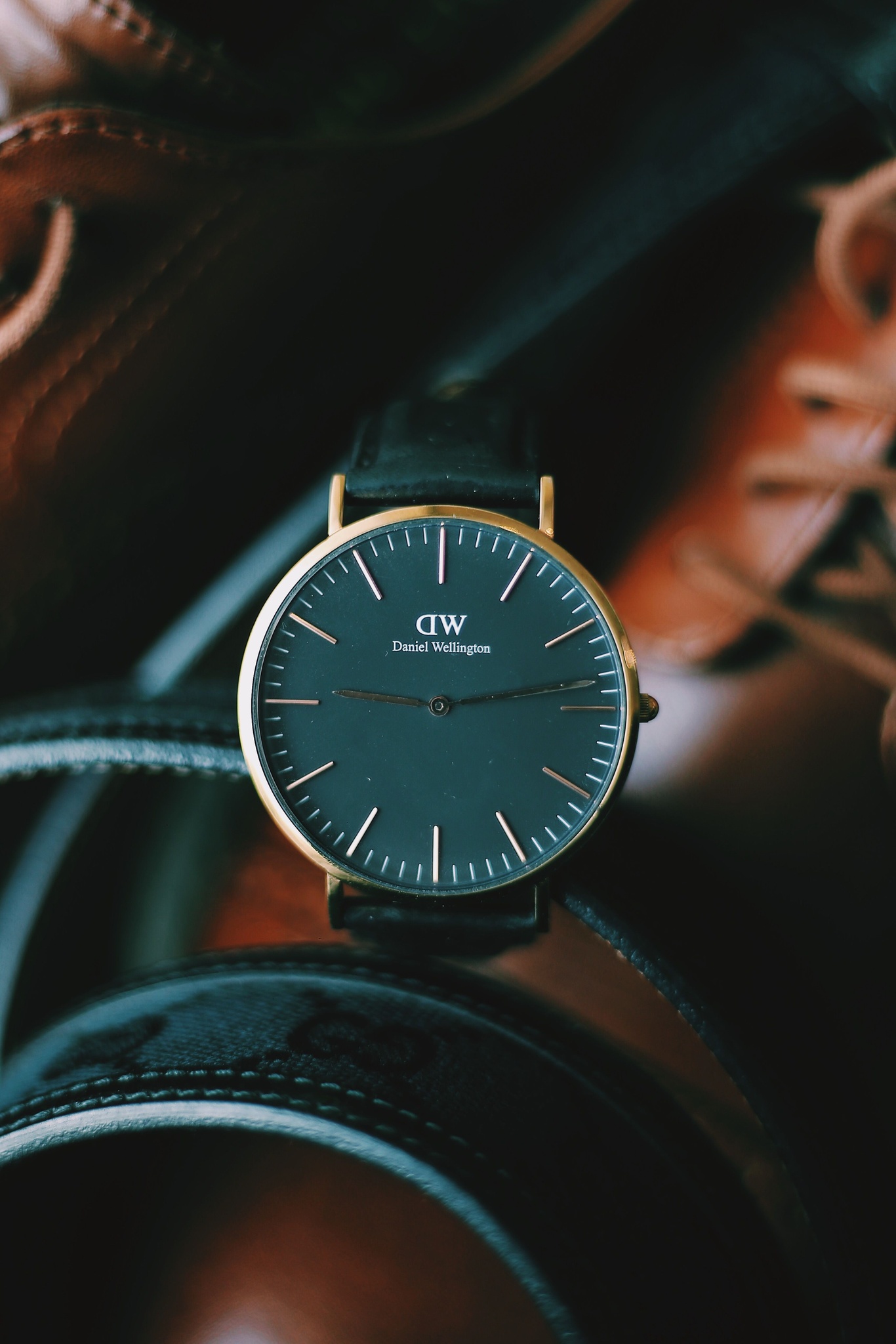 Gold cased watch with a black dial resting on a black leather belt